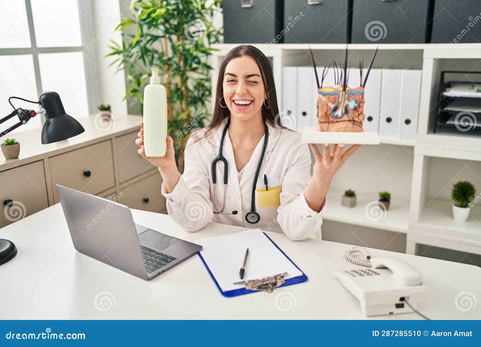 hispanic doctor woman holding model of human anatomical skin and hair winking looking at the camera with sexy expression, cheerful