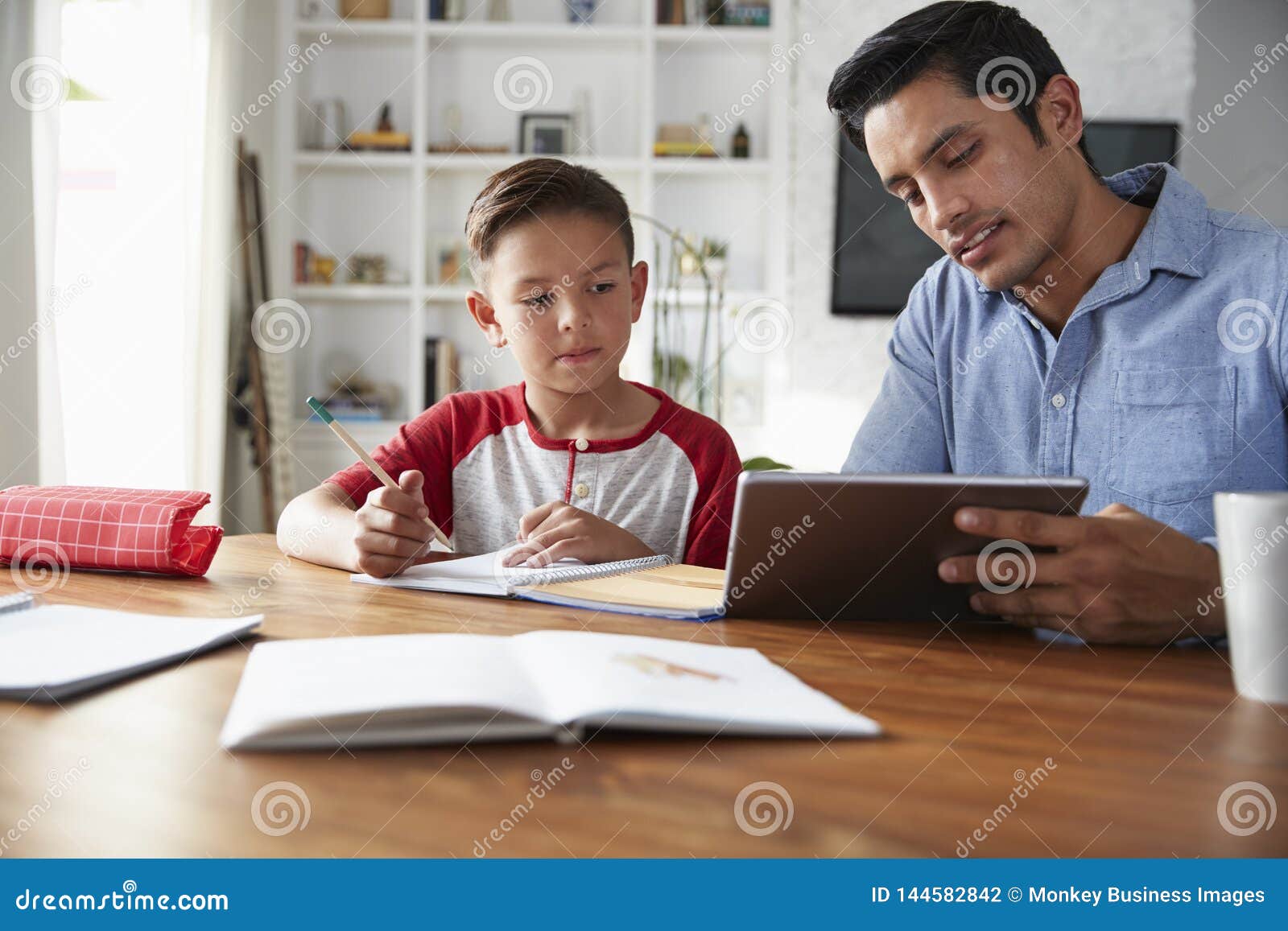 hispanic pre-teen boy sitting at table working with his home school tutor, using tablet computer