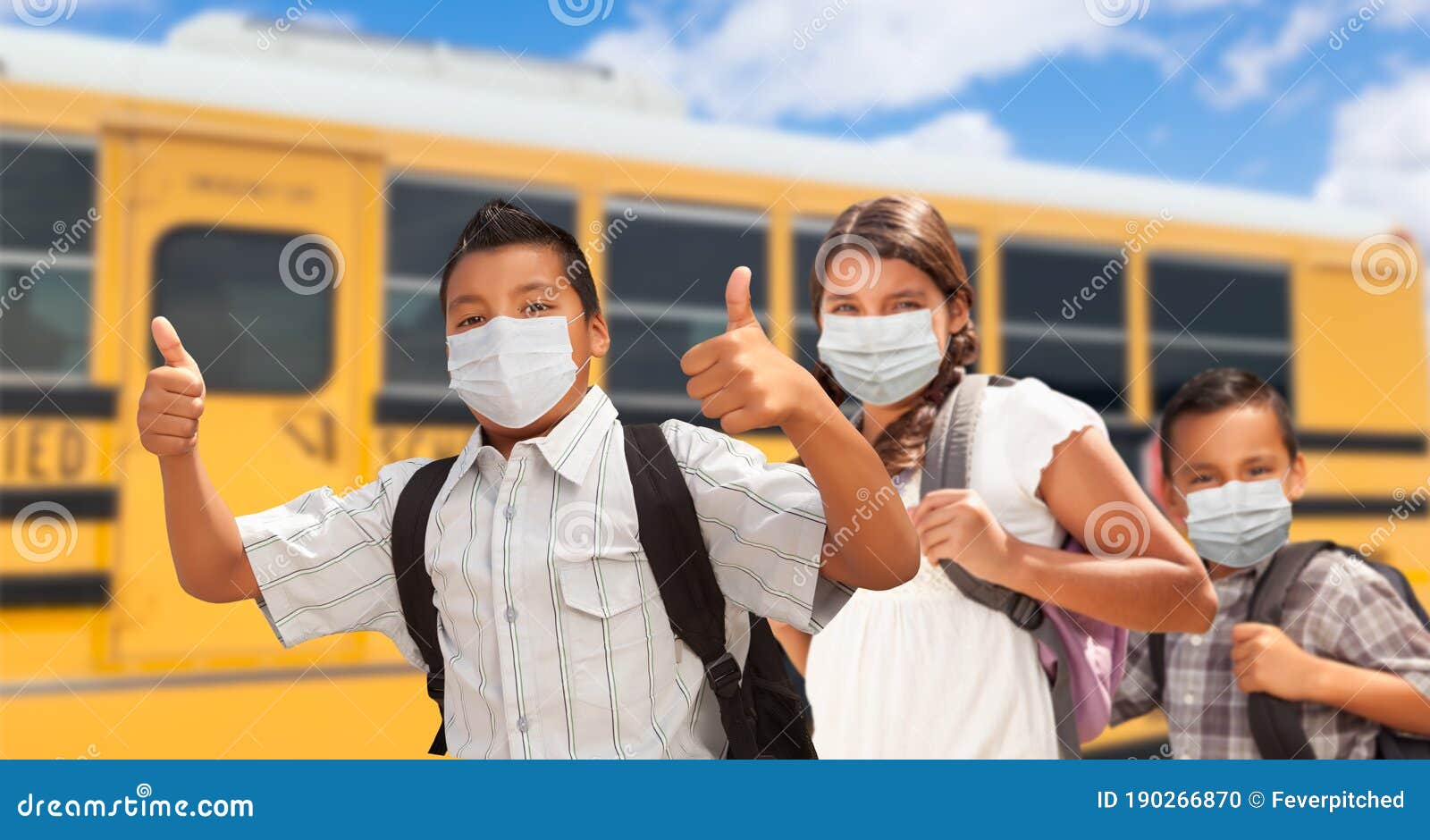 three hispanic students near school bus wearing face masks