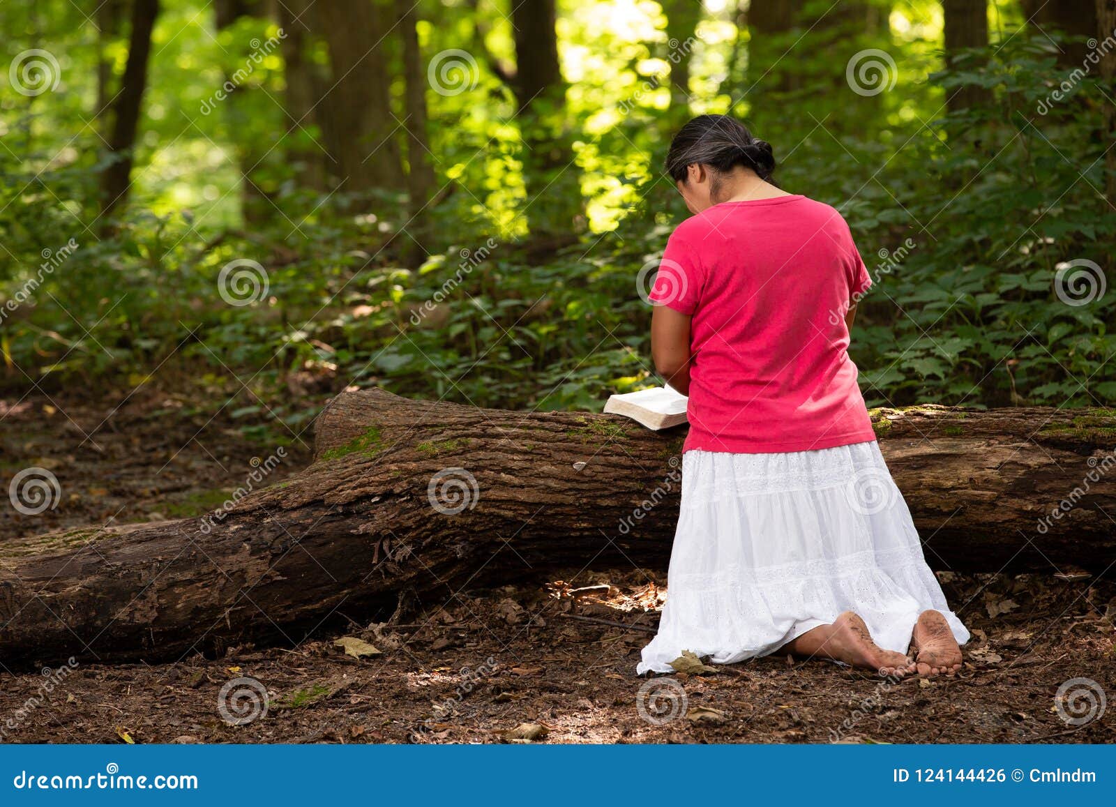 woman in forest preserve with bible kneeling in prayer