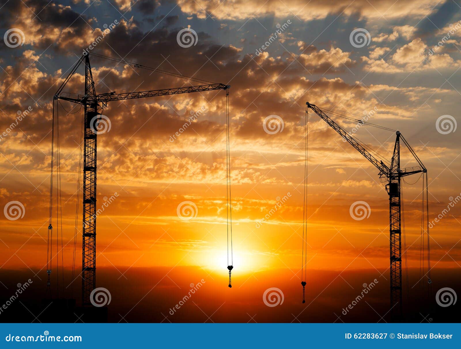 hoisting cranes working on beautiful cloudy sky with orange sunset