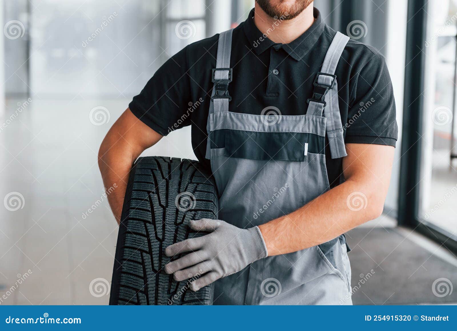 Holding Tire. Man in Uniform is Working in the Autosalon at Daytime