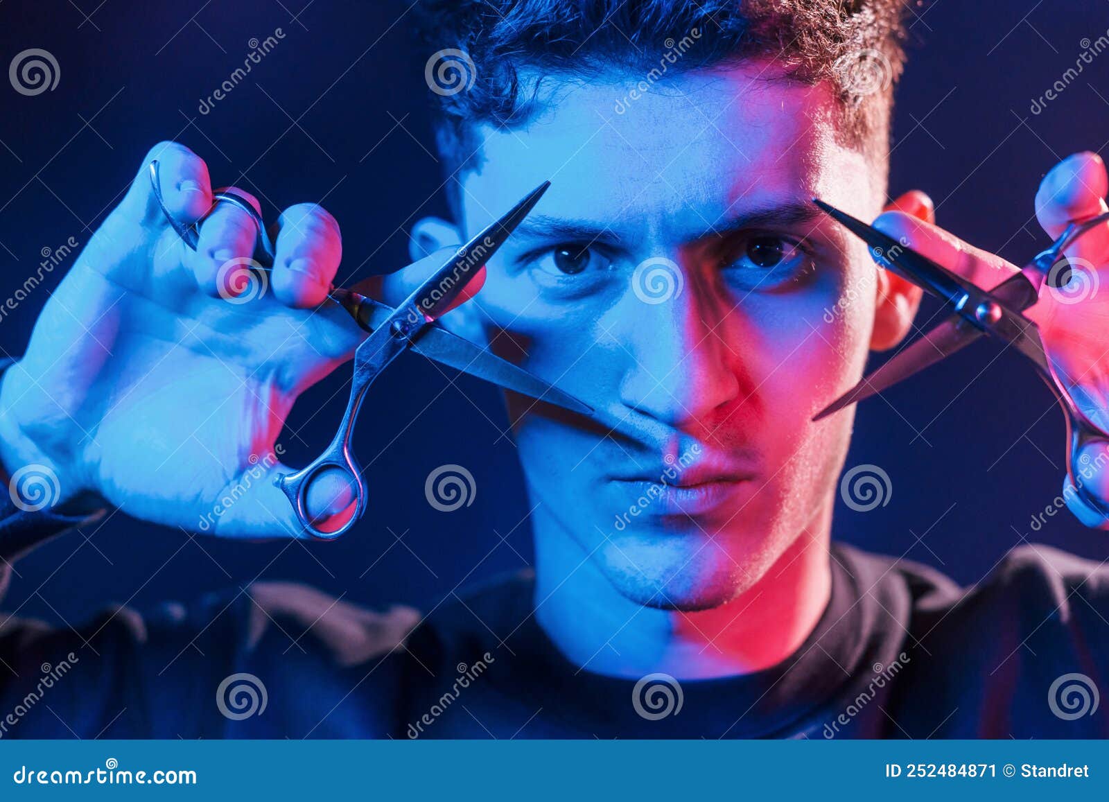 Holds Scissors. Young Barber with Work Equipment Standing in the Studio with Neon Lighting Stock