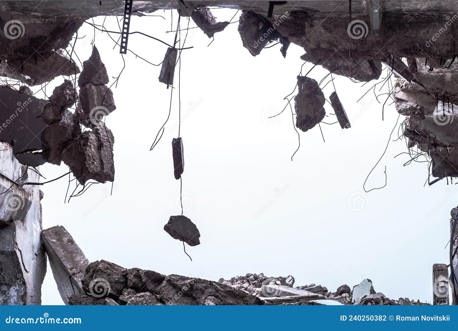 a hole in the body of a building with a pile of construction debris and concrete fragments hanging on the rebar against