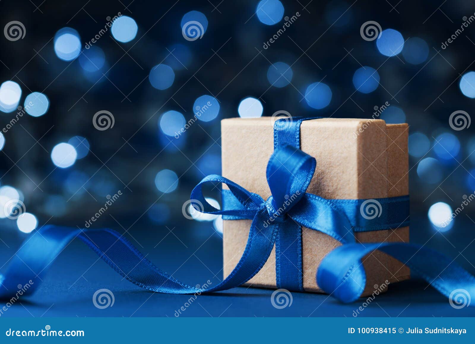 holiday gift box or present with bow ribbon against blue bokeh background. magic christmas greeting card.