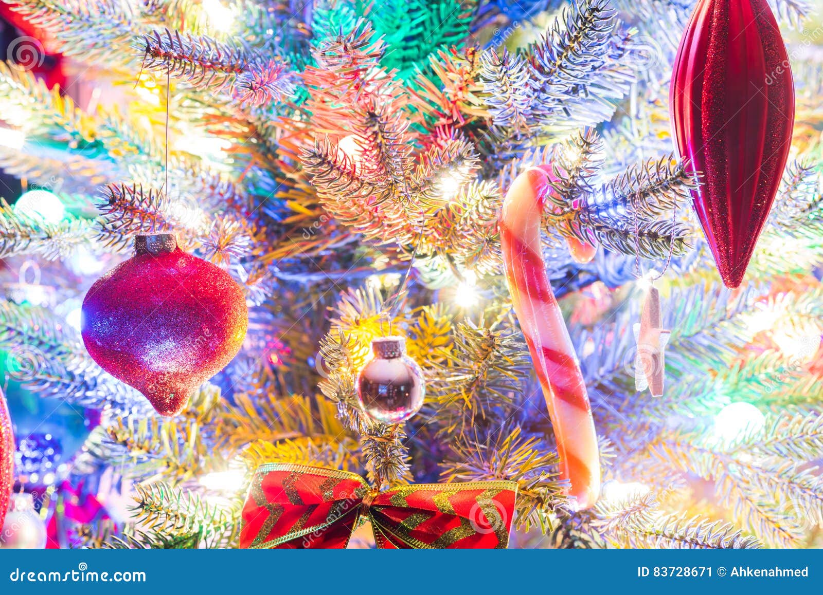 holiday season, christmas tree decorations glow under luminous and vivid, colorful lights on a small faux indoor tree.