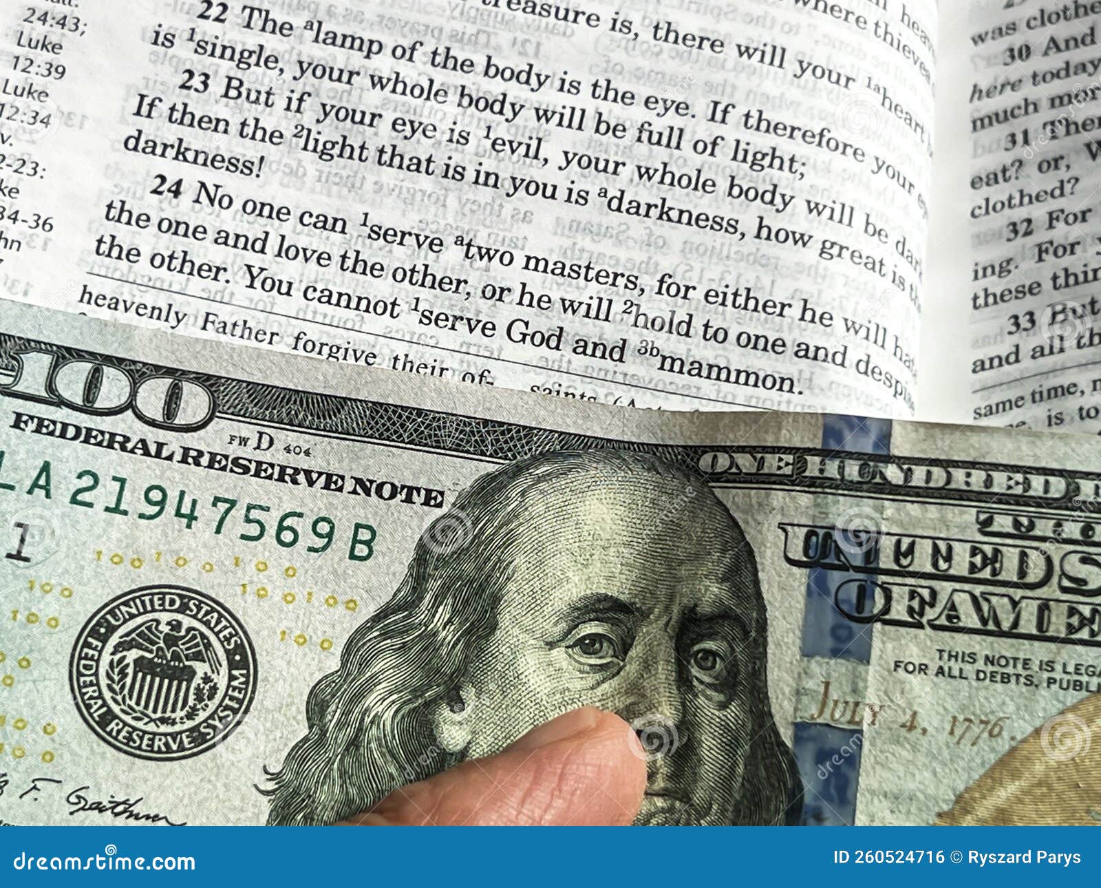 the holy bible in english with a tab from the $ 100 banknote showing a passage from the gospel according to st. matthew 6:24