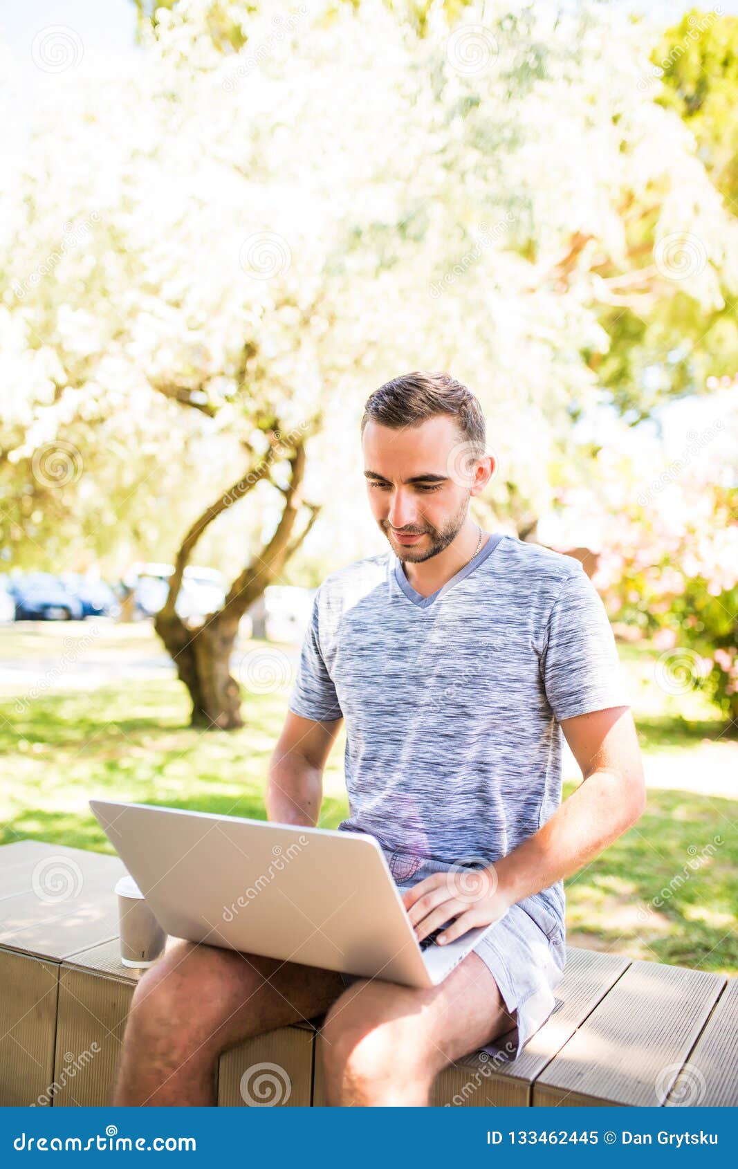 Hombre caucásico hermoso que usa sentarse del ordenador portátil al aire libre en un parque Día de la sol del verano Concepto de. Hombre caucásico hermoso que usa sentarse del ordenador portátil al aire libre en un parque Concepto de hombres de negocios jovenes que trabajan en inicio