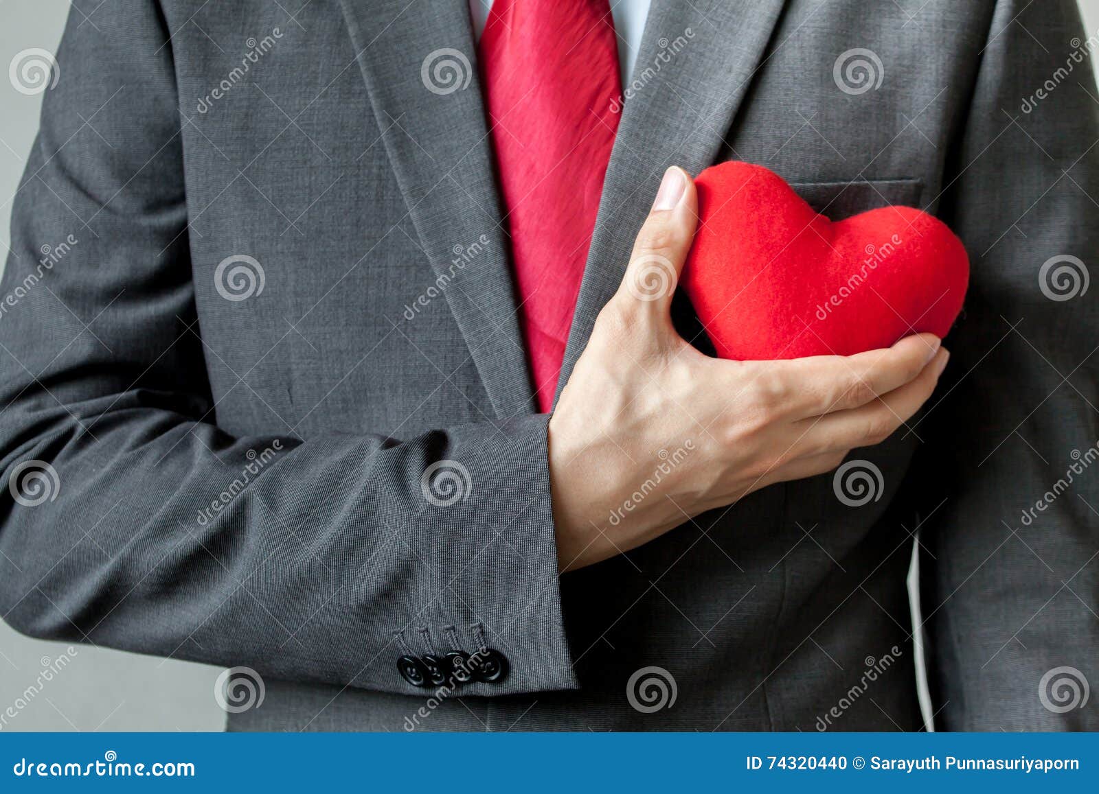 Hombre de negocios que muestra la compasión que lleva a cabo el corazón rojo sobre su pecho en su traje - crm, concepto del negocio de la mente del servicio