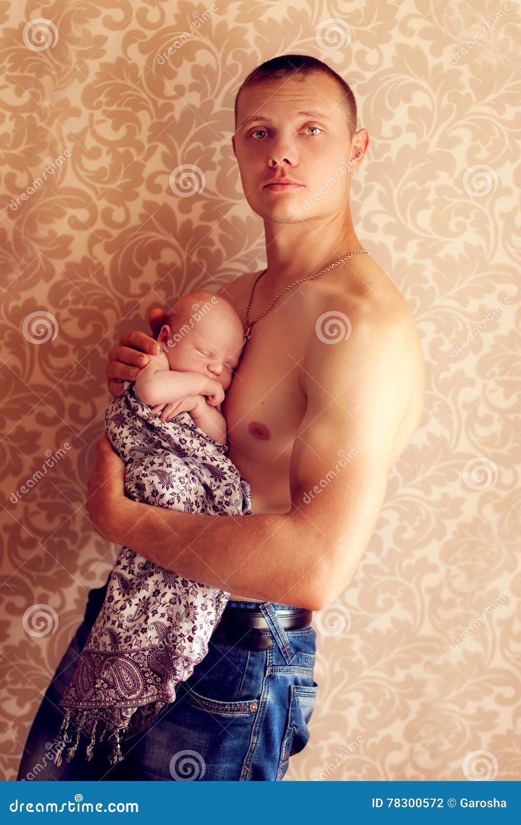 Hombre fuerte joven que detiene a un pequeño bebé frágil en sus brazos. Hombres fuertes jovenes que detienen a un pequeño bebé frágil en sus brazos Culturista del atleta que presenta con el hijo recién nacido