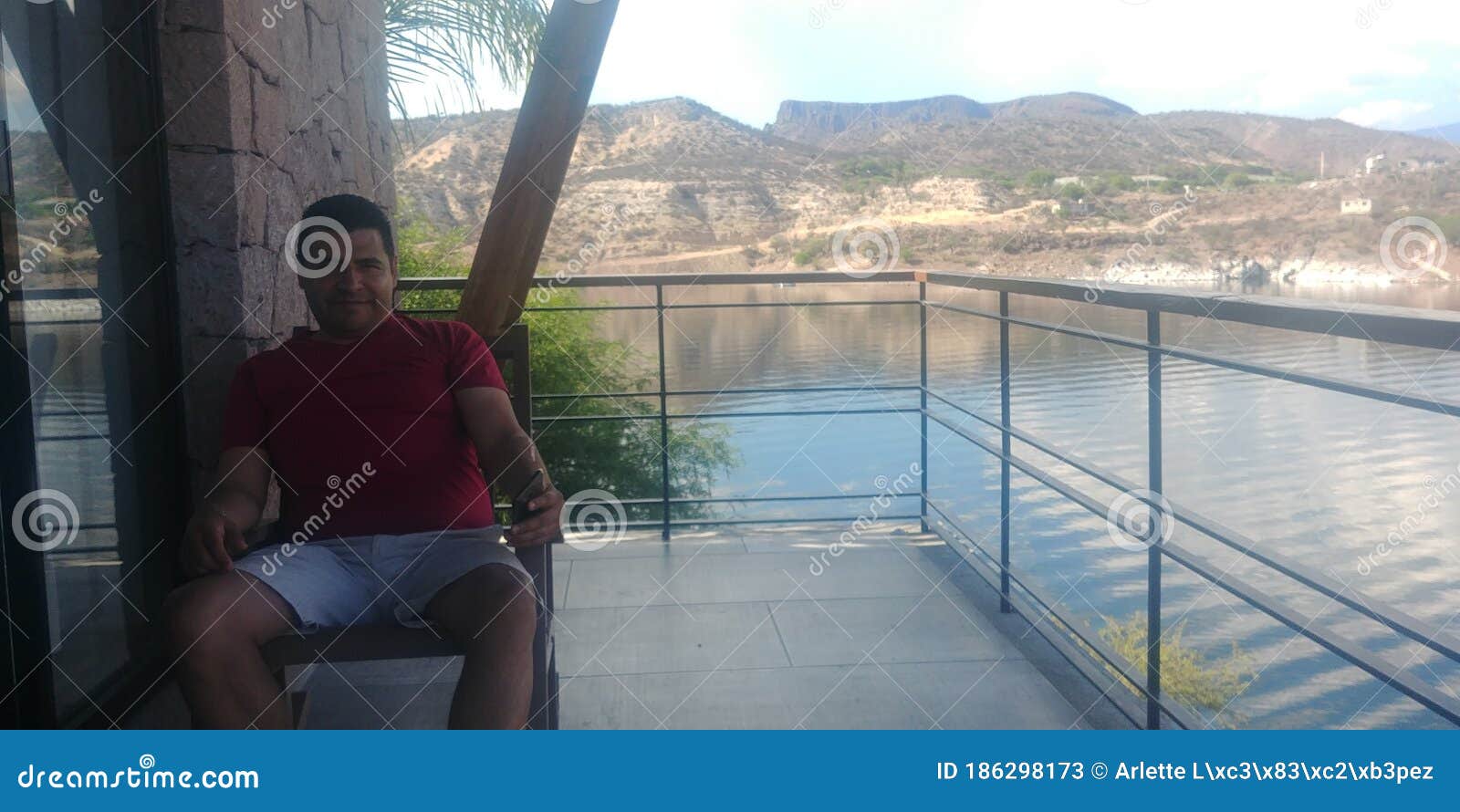 hombre latino con vista de lago y montaÃÂ±a desde la terraza con mesa y sillas de madera al amanecer