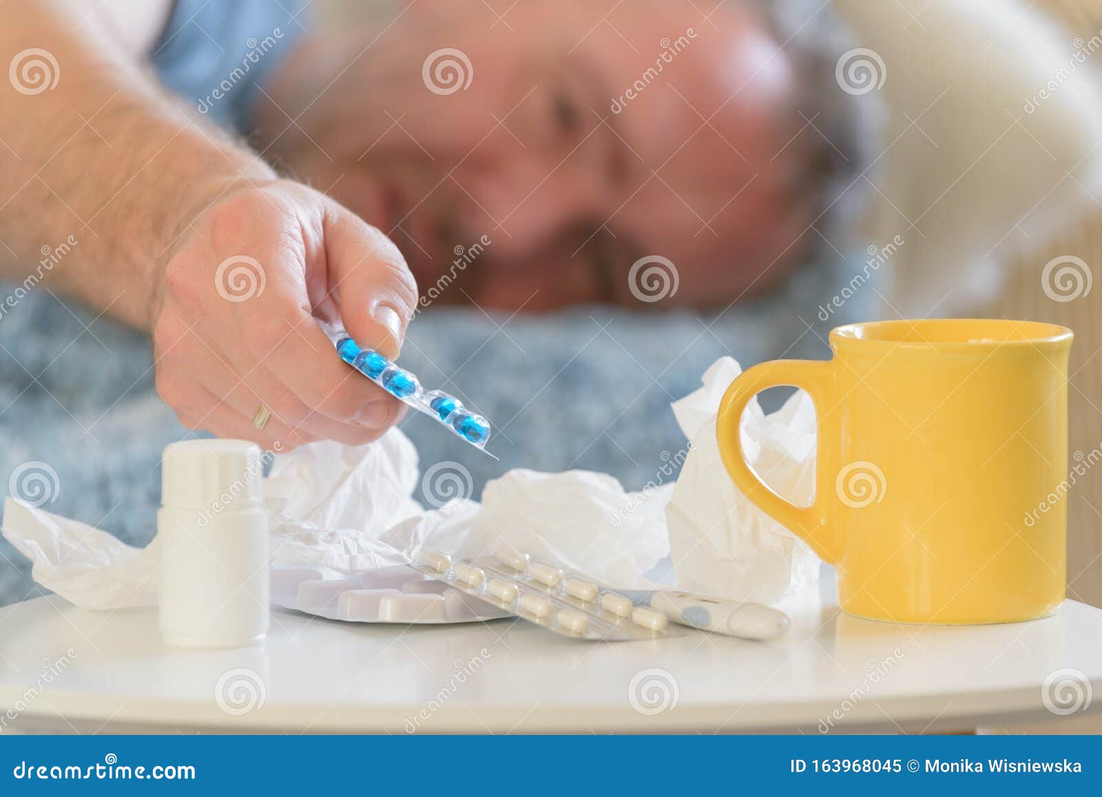 Hombre maduro que padece gripe o frío. Hombre que sufre de gripe o de frío está tristemente cubierto con una manta en su cama Medicamentos, medicamentos, vasos y tejidos en primer plano