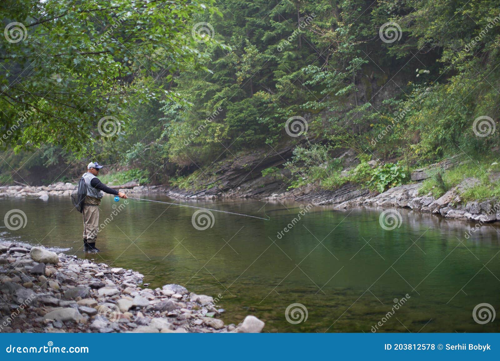 Hombre Tirando Barras De Pesca Al Río De Montaña Foto de archivo