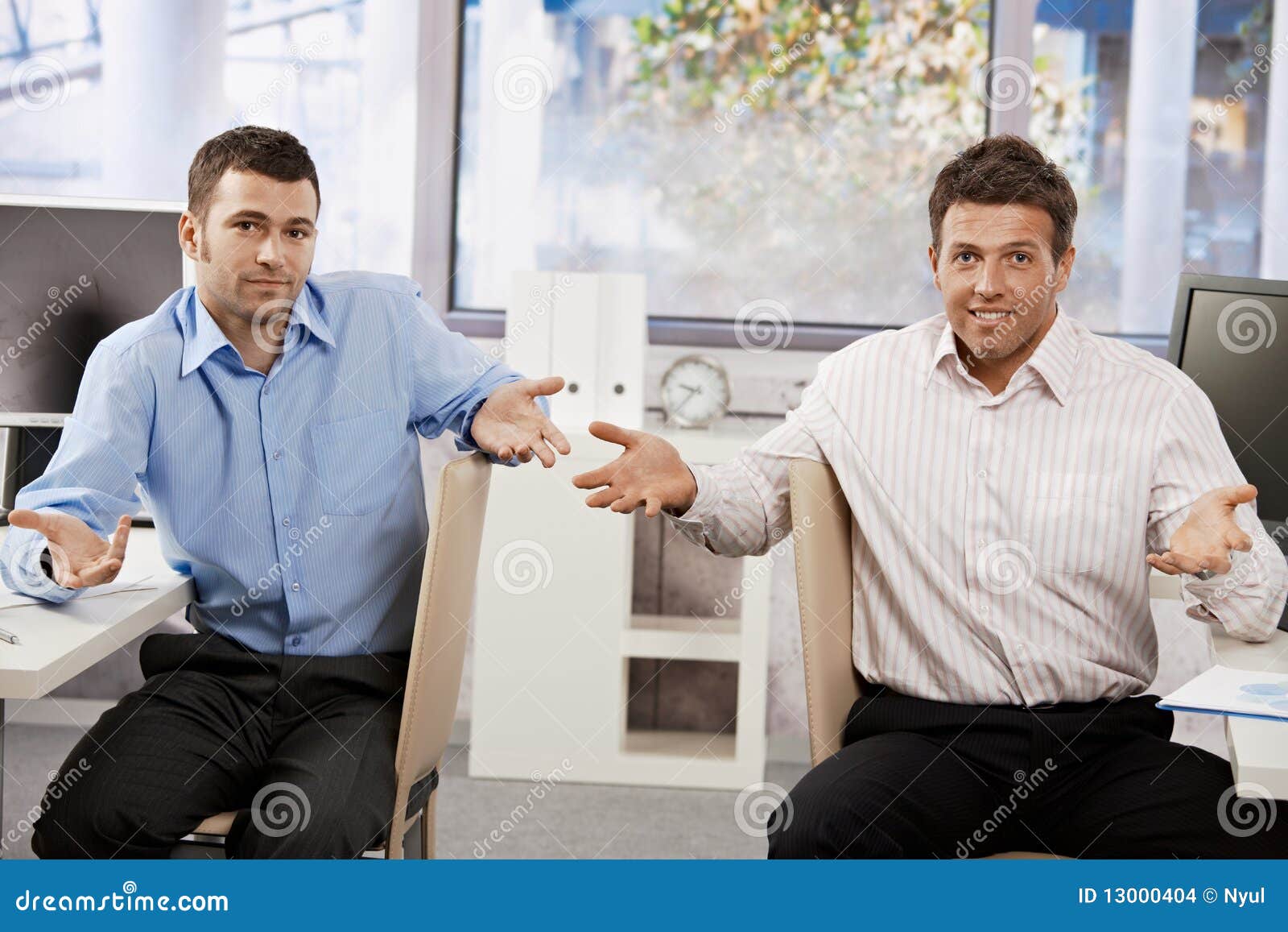 Hombres de negocios confusos. Dos hombres de negocios que se sientan en la oficina que mira la cámara confundida, manos speading.
