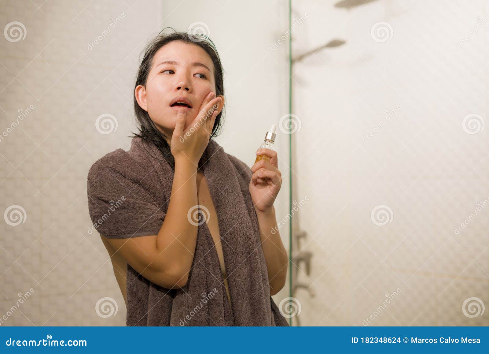 young beautiful and happy asian chinese woman applying serum facial skin care and face treatment in the bathroom enjoying morning