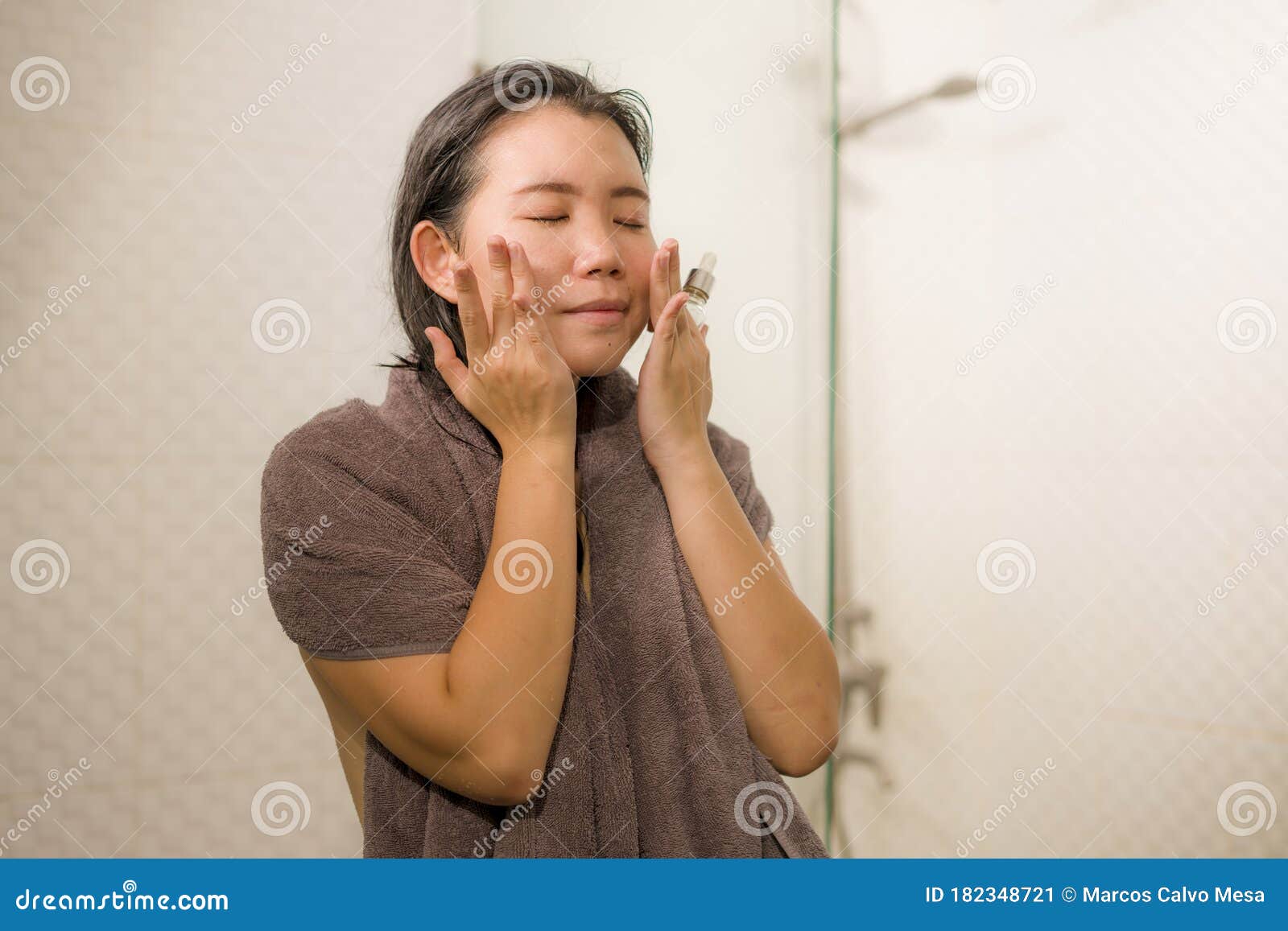 young beautiful and happy asian korean woman applying serum facial skin care and face treatment in the bathroom enjoying morning