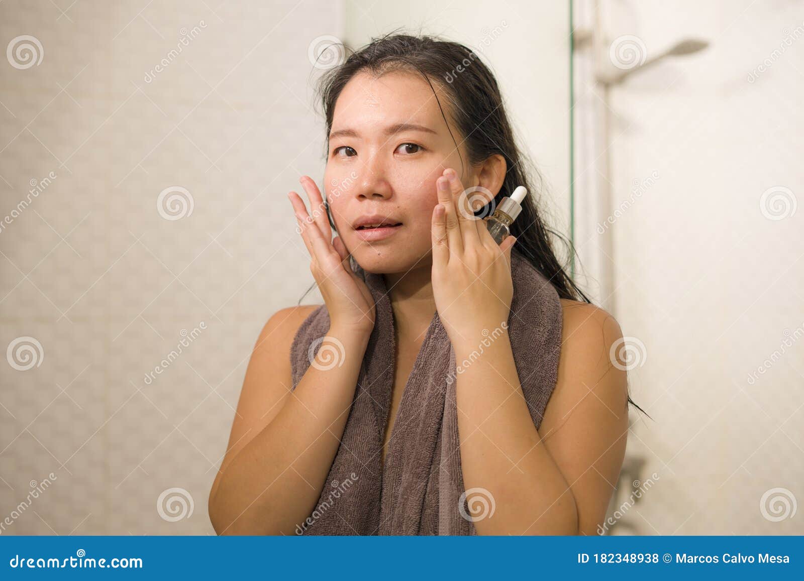 young beautiful and happy asian korean woman applying serum facial skin care and face treatment in the bathroom enjoying morning