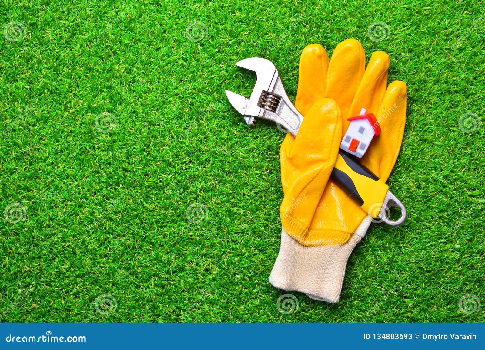home repairs concept. building glove with a adjustable wrench and miniature house on a green grass.