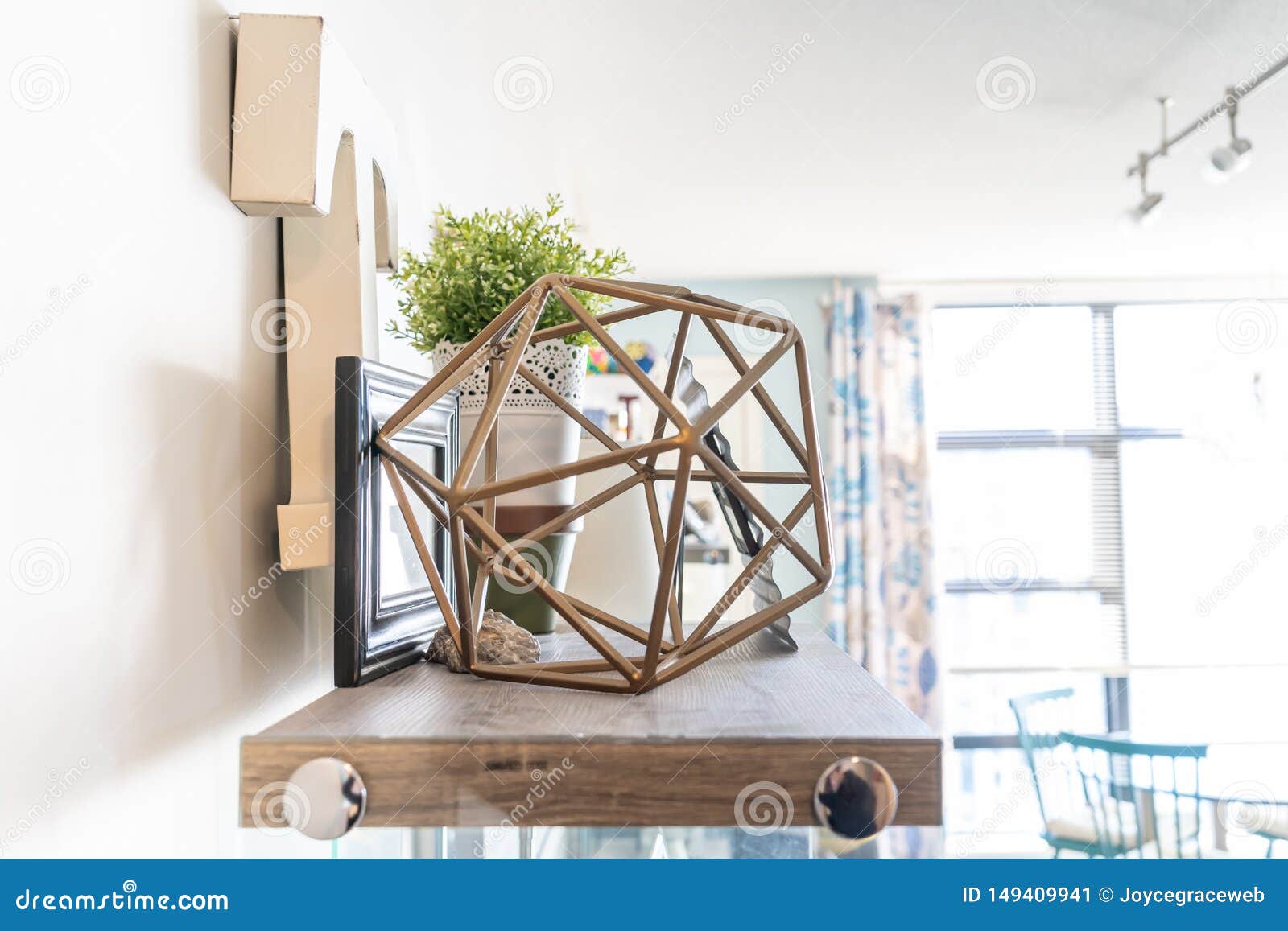 home shelf with decorative knick knacks, including a geometric wire object, a letter `t`, picture frames and a planter. bright liv