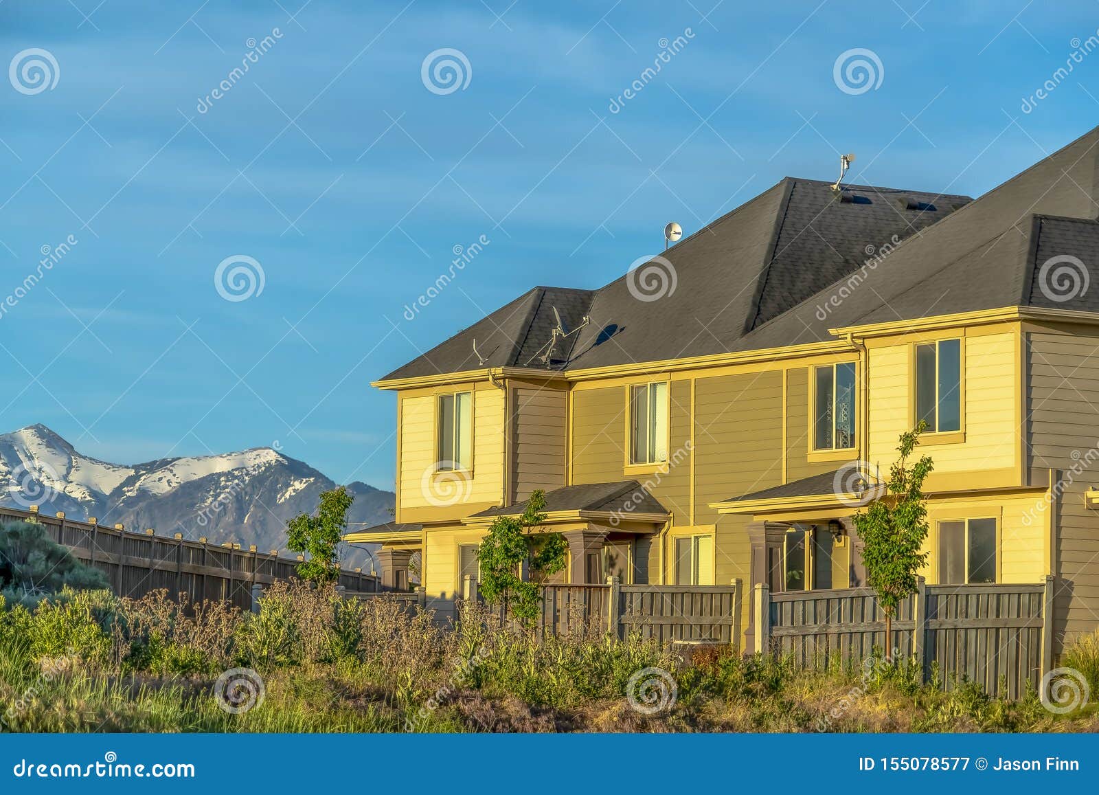 Home With Wooden Fence And View Of Snowy Mountain Peak Against Blue Sky
