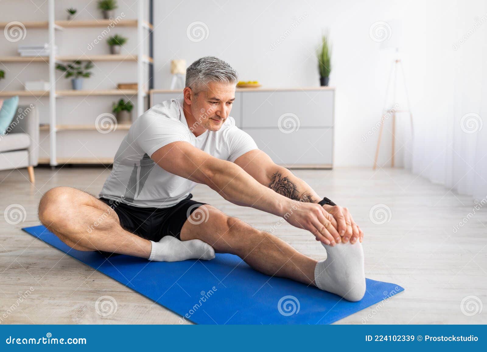 Flexibility exercises. Athletic young woman doing yoga on mat, stretching  her legs during home Stock Photo by Prostock-studio
