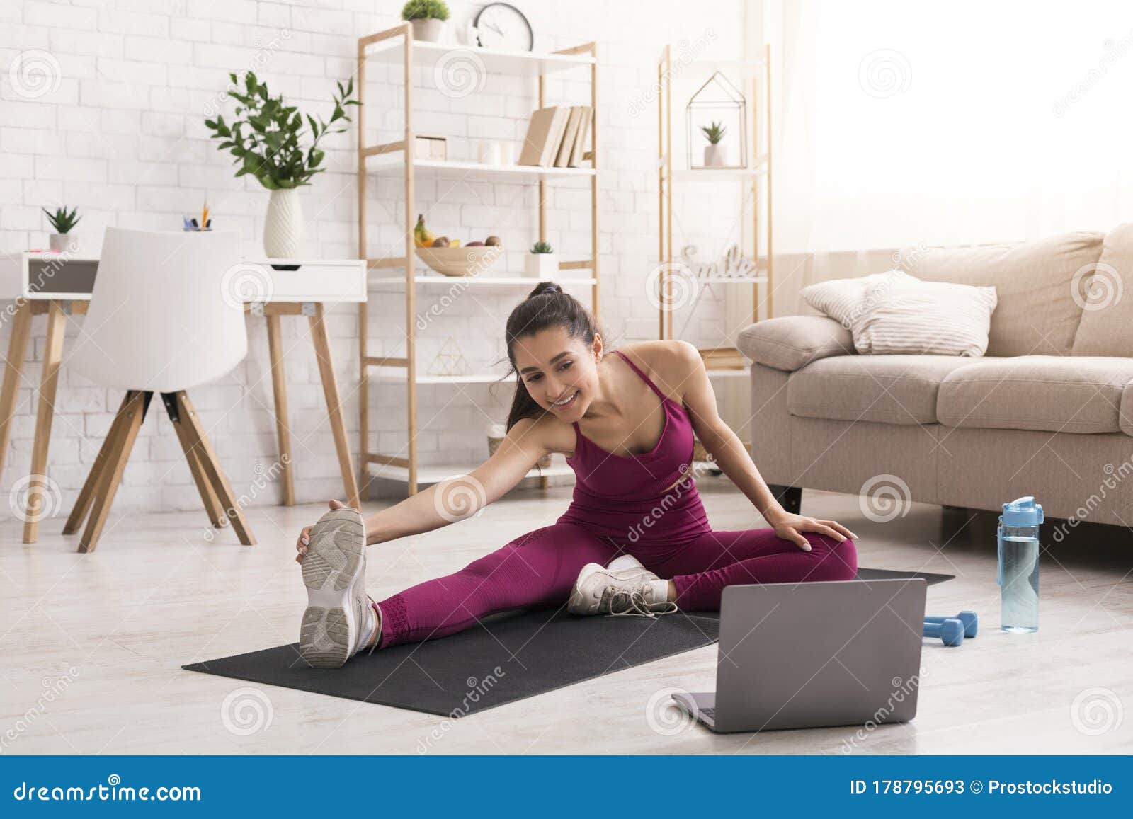 Fit woman doing yoga exercise while watching tutorial on laptop at