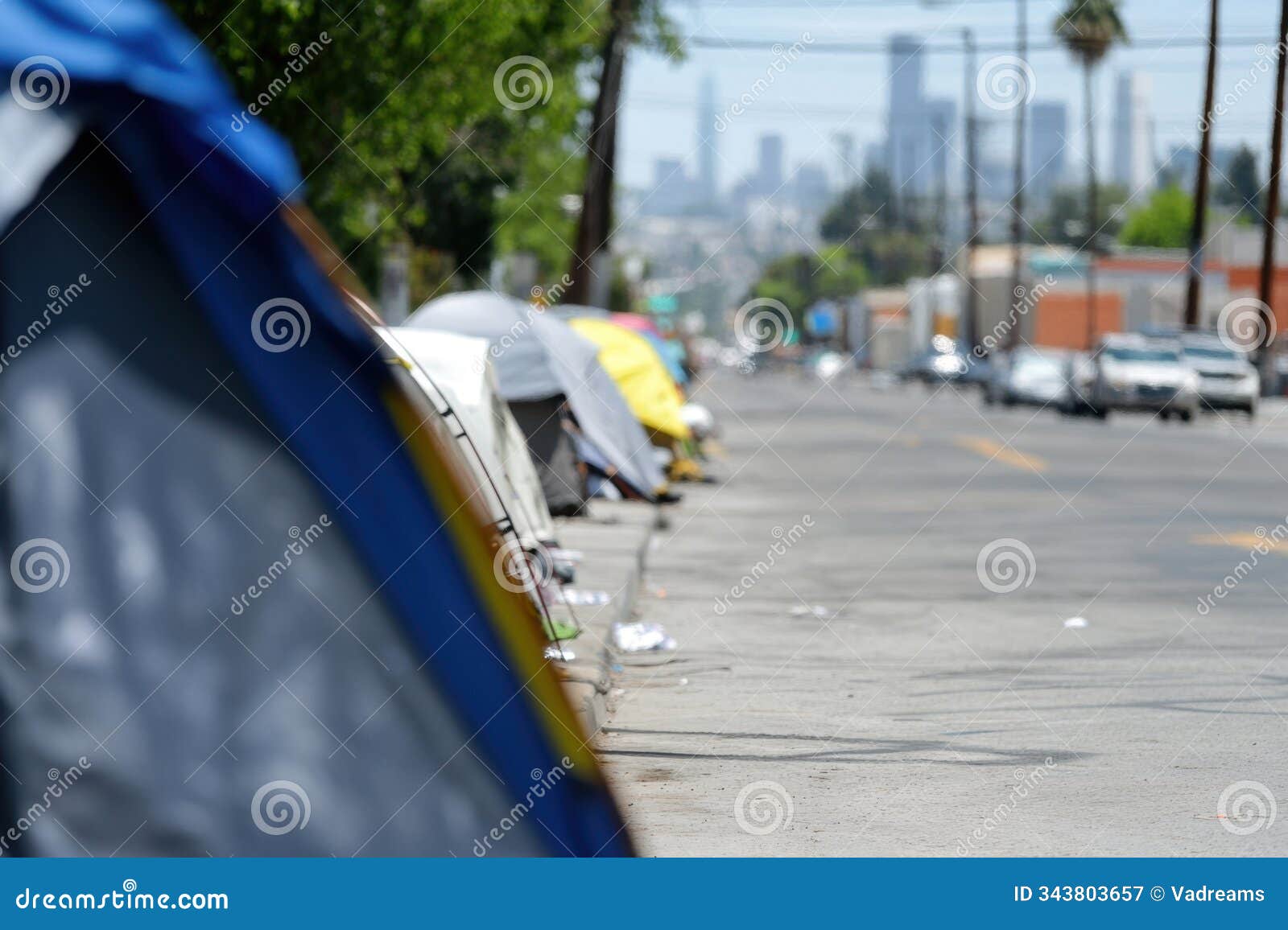 homeless camp is set up on city street. row of tents forms an encampment for homeless people, with modern city