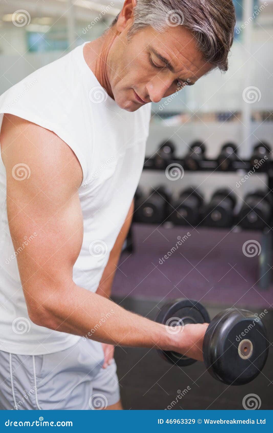 Homem apto que levanta o peso preto pesado no gym