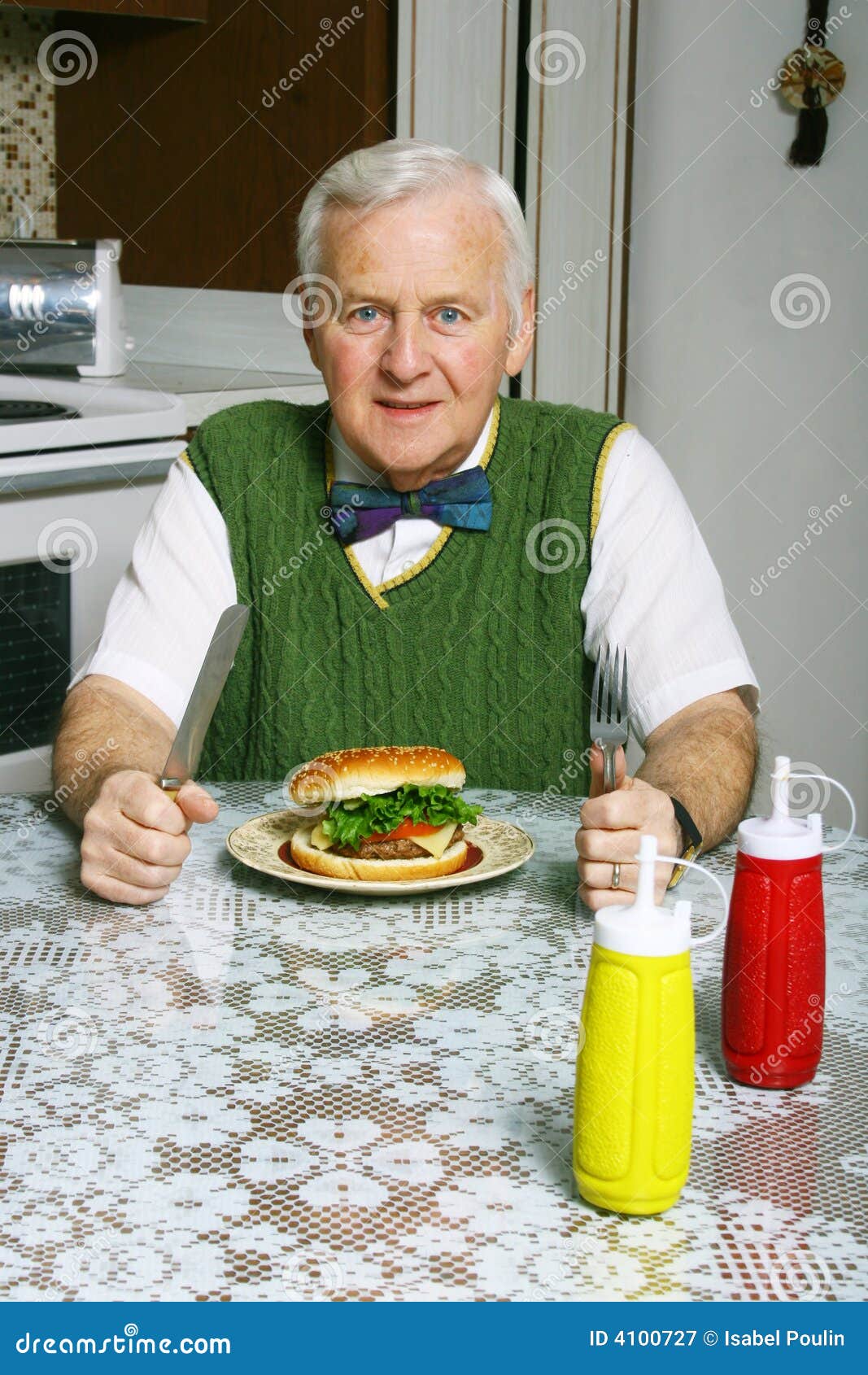 Homem com fome. Um homem sênior que senta-se em uma tabela com um Hamburger na frente dele em uma placa.