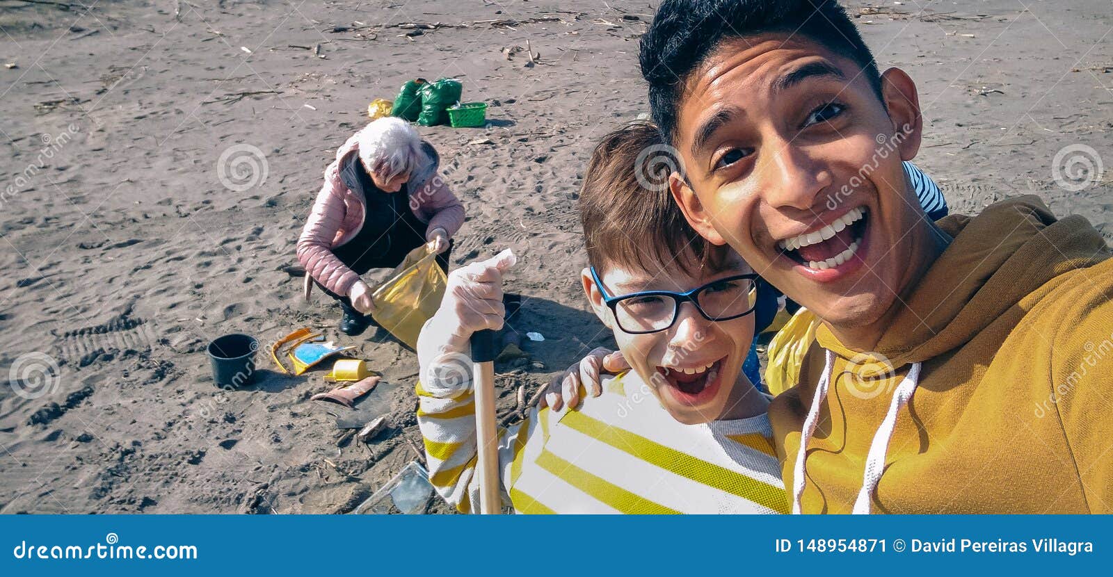 Homem novo e menino que tomam o selfie quando grupo de volunt?rios que limpam a praia. Homens novos e menino que tomam o selfie com grupo m?vel do quando de volunt?rios que limpam a praia