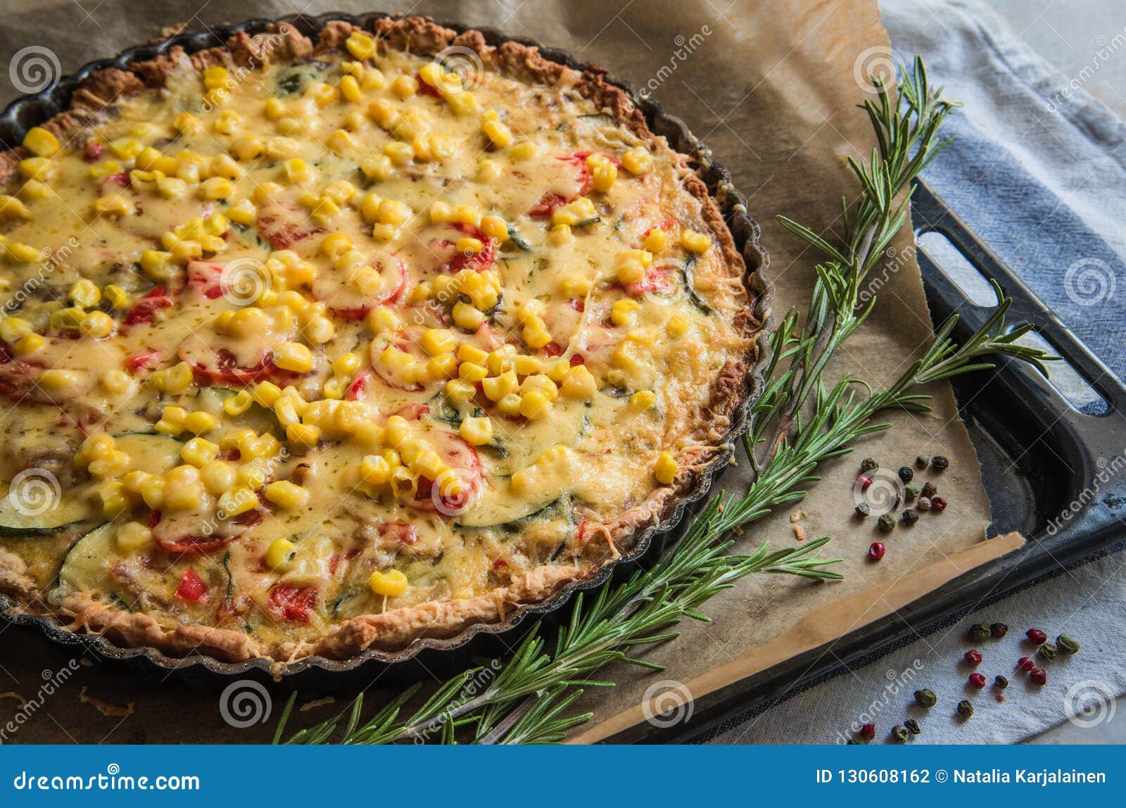 Homemade pie with zucchini, tomatoes, cheese and corn on a tray, with fresh rosemary and colored pepper. Homely style