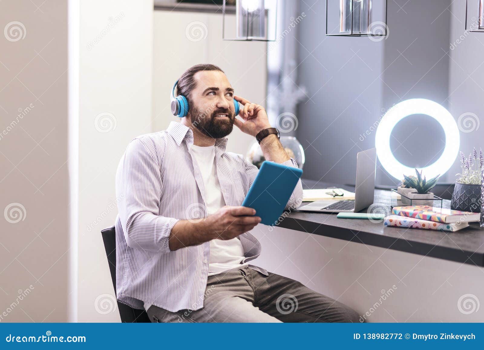 Homme barbu aux cheveux foncés dans des écouteurs écoutant la musique sur un comprimé. Écouter la musique écouteurs de port d'homme barbu aux cheveux foncés écoutant la musique sur un comprimé