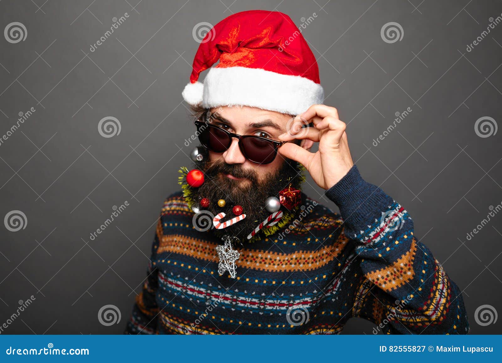 Homme dans le chapeau et des lunettes de soleil de Santa au-dessus de fond gris Lunettes de soleil masculines barbues de fixation et regard à l'appareil-photo