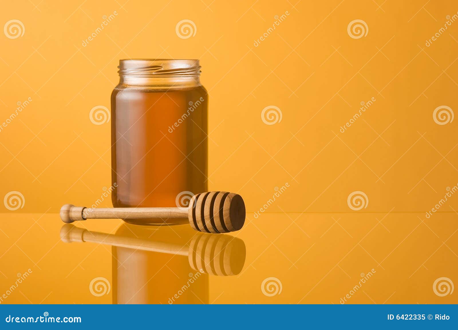 Honey jar and dipper with reflection on orange background. Space for text