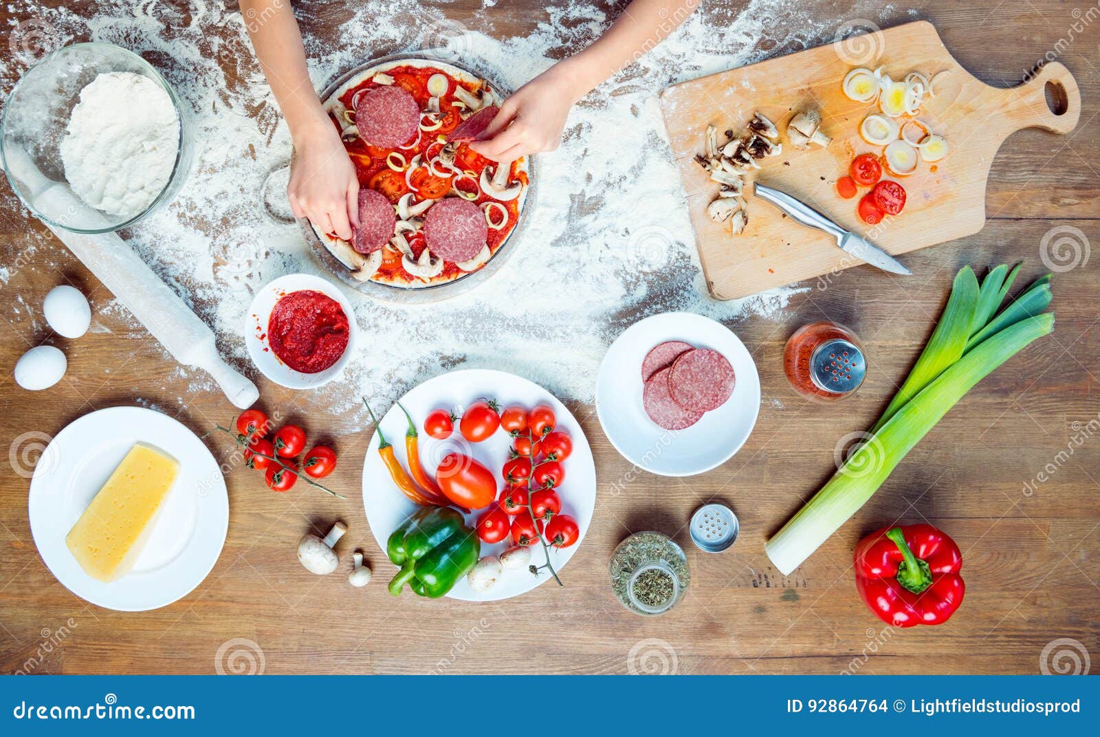 Hoogste mening die van kind pizza met pizzaingrediënten, tomaten, salami en paddestoelen maken op houten tafelblad