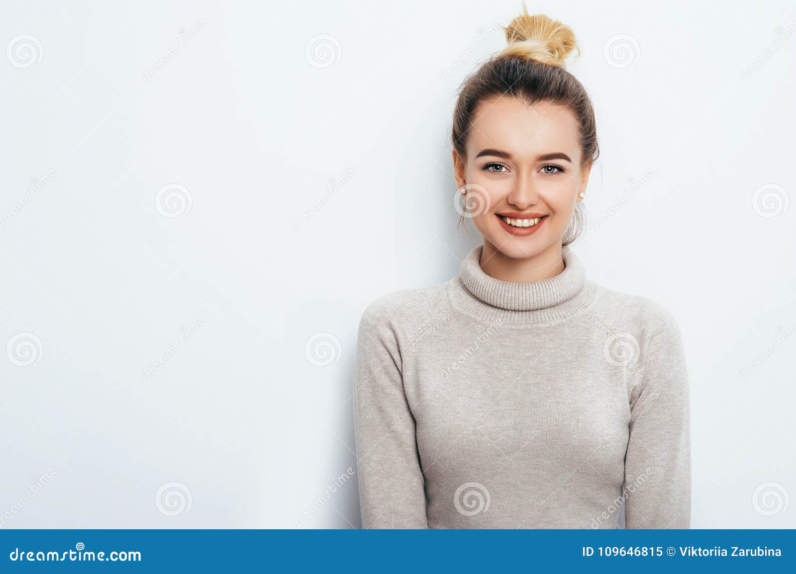 horizontal portrait of cheerful woman with appealing smile, having hair bun wearing in sweater  over white background.