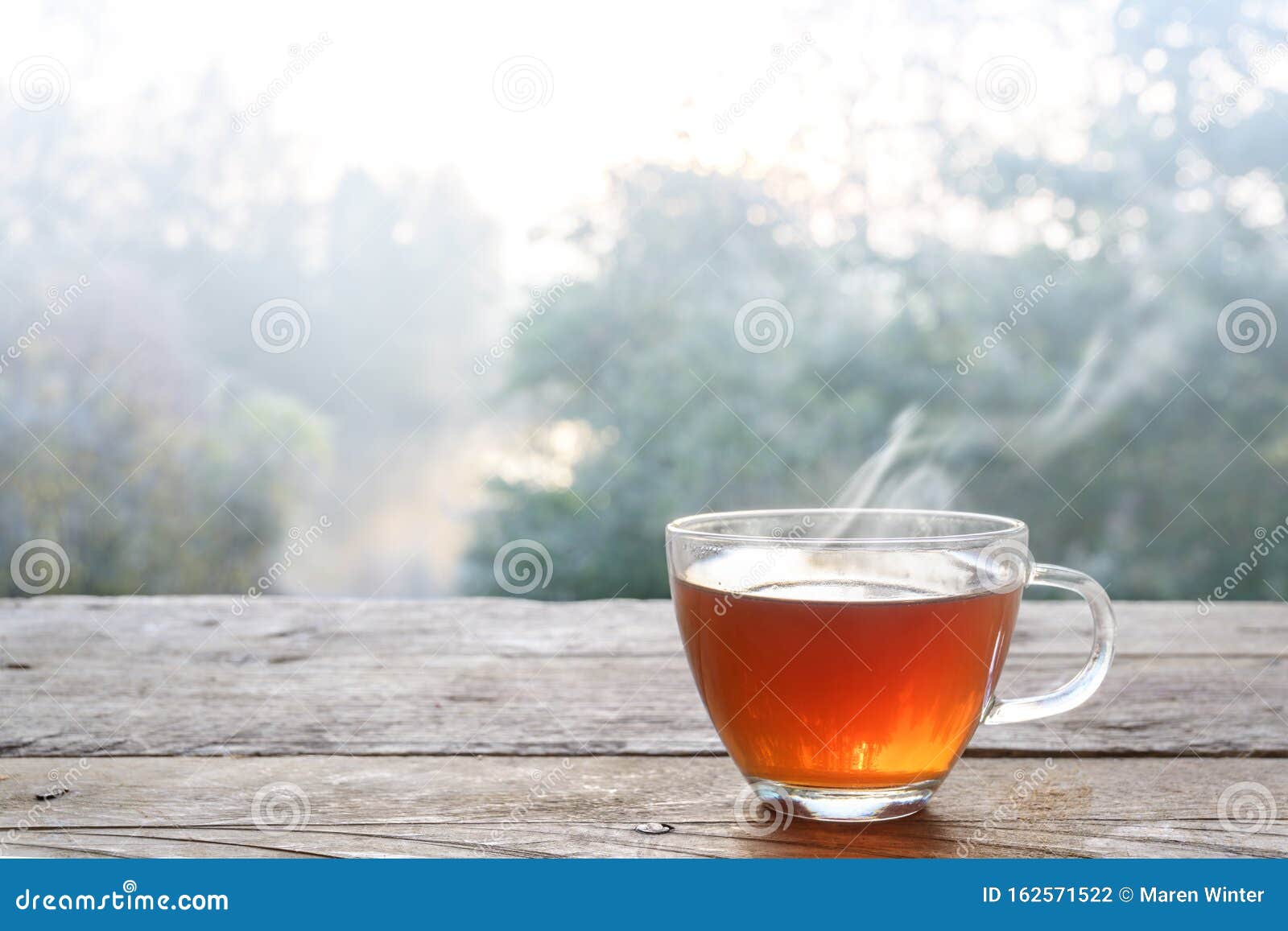 hot steaming tea in a glass cup on a rustic wooden outdoor table on a cold foggy winter day, copy space, selected focus, narrow