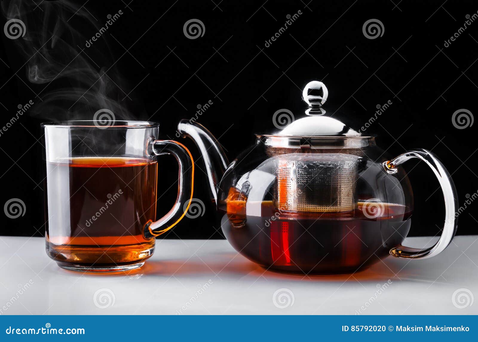 Hot Tea in Glass Teapot and Cup with Steam on White Surface Stock Photo