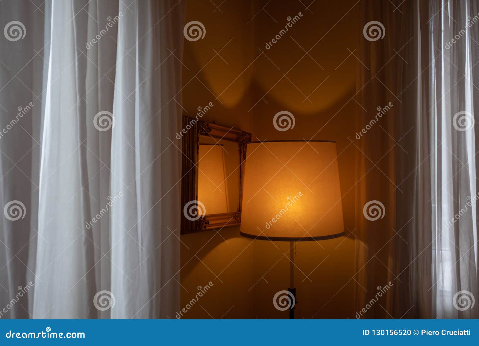 hotel room with orange lit abat-jour, framed mirror and white curtains