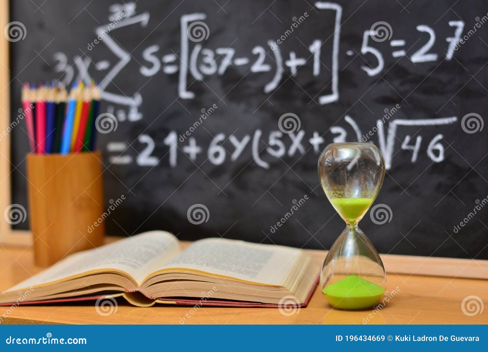 hourglass and book on a table, with a blackboard background