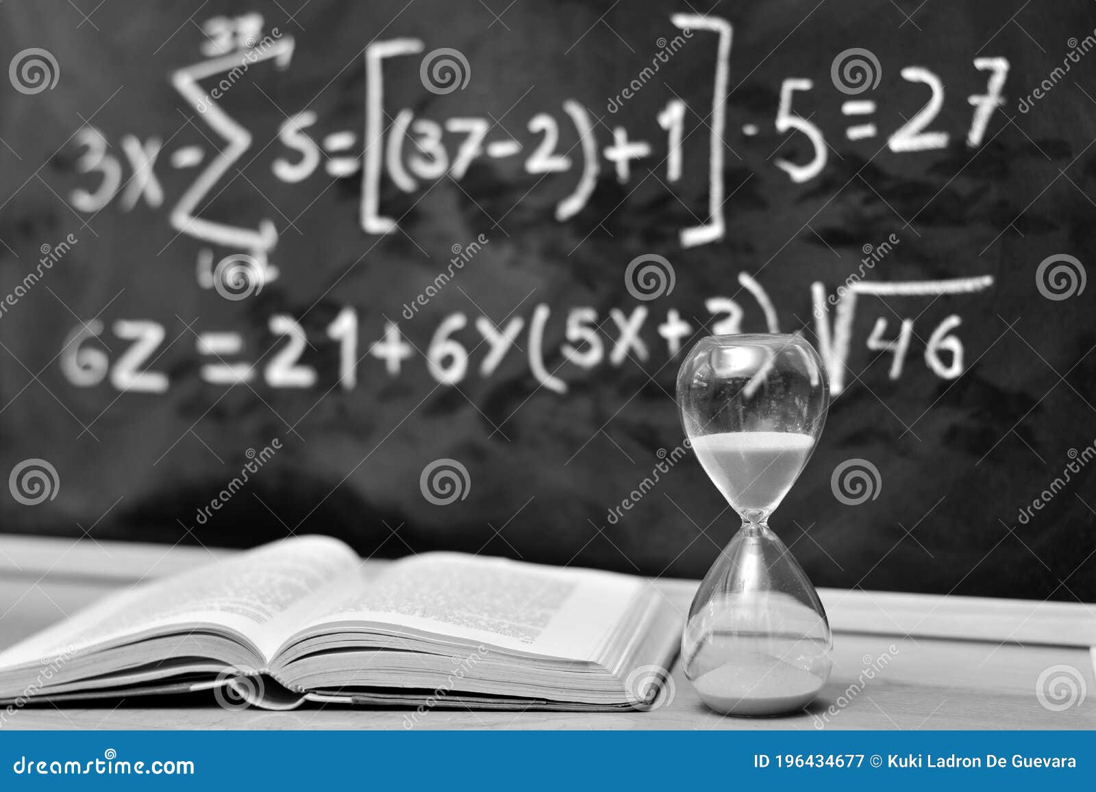 hourglass and book on a table, with a blackboard background