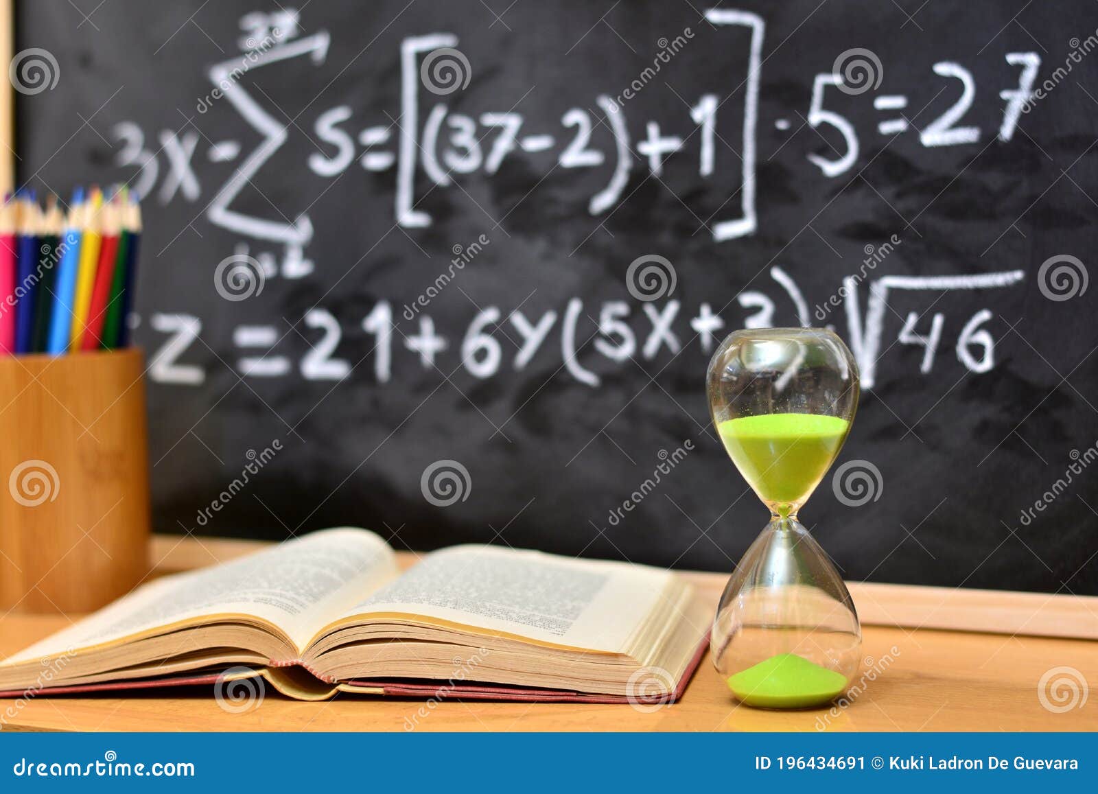 hourglass and book on a table, with a blackboard background