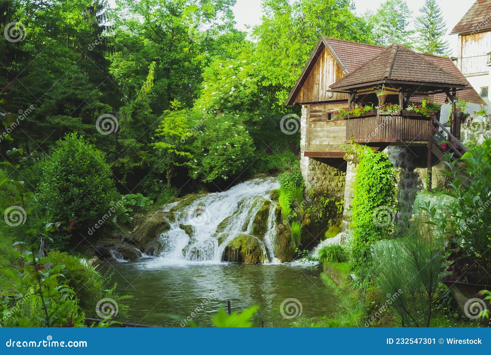 House with a Small Waterfall Pouring Down To River Surrounded by Trees