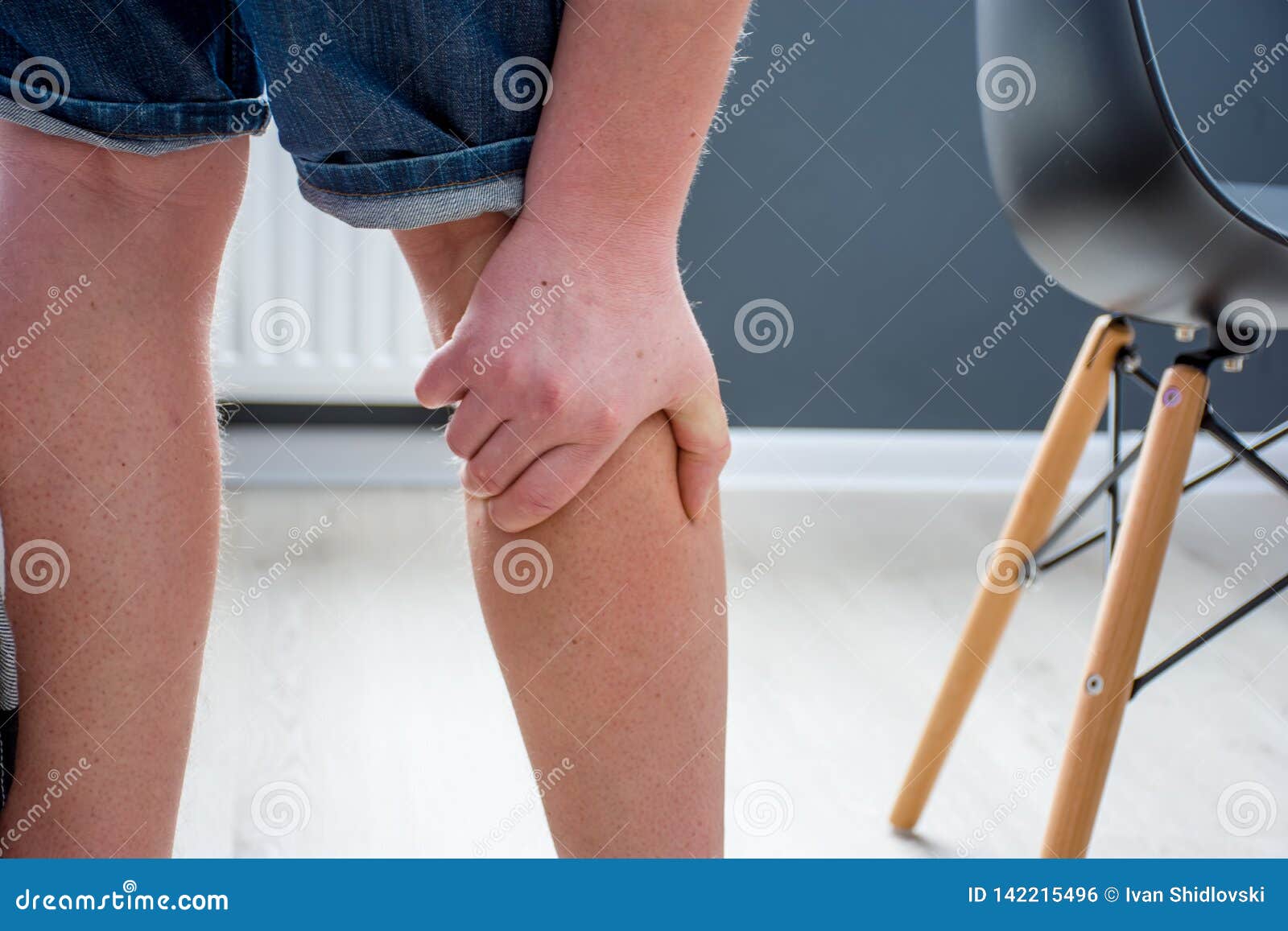 human, who had been elevated from chair, holding his palm over calf or gastrocnemius muscle, which grabbed cramp with severe pain.
