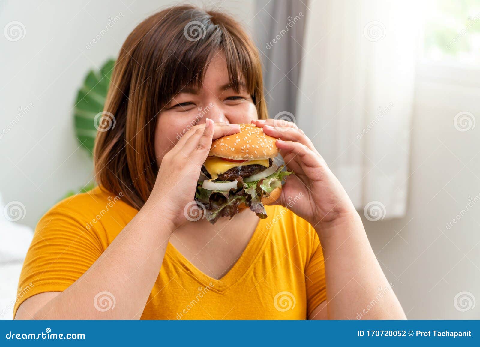 hungry overweight young asian woman holding hamburger, her hungry all time and overeat, gluttony and binge eating. her lifestyle