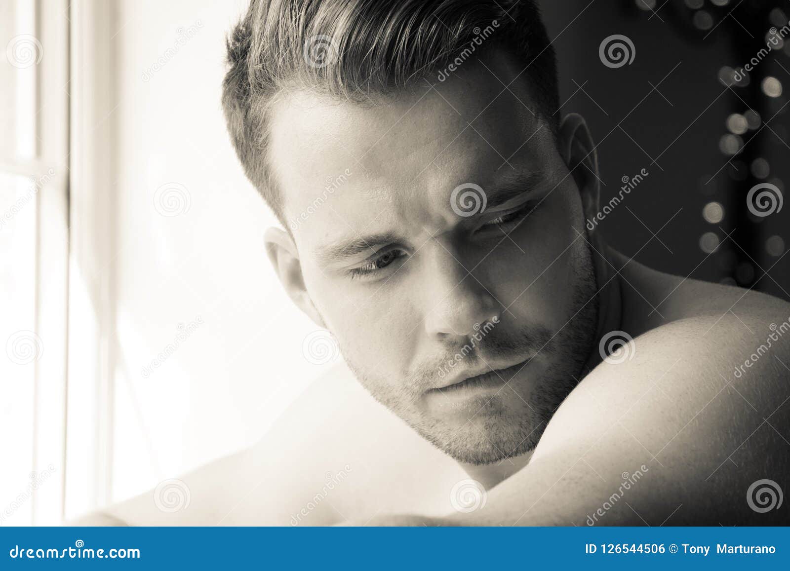 hunky muscular, shirtless man with defined abs and muscles looks out of window