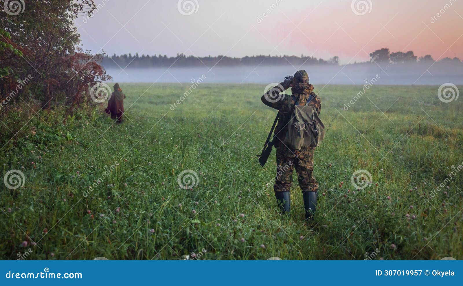 huntsman and hunter look through binoculars through the fog at wild ungulates