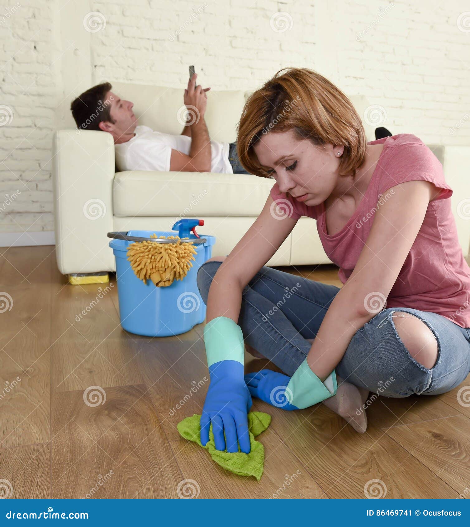 husband resting on couch while wife cleaning doing housework in chauvinism concept