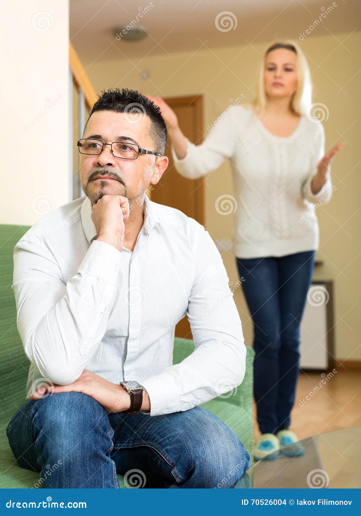 Husband tired of his wife. Husband is sitting on a sofa tired of his wife and turned away from her. His wife is nagging him