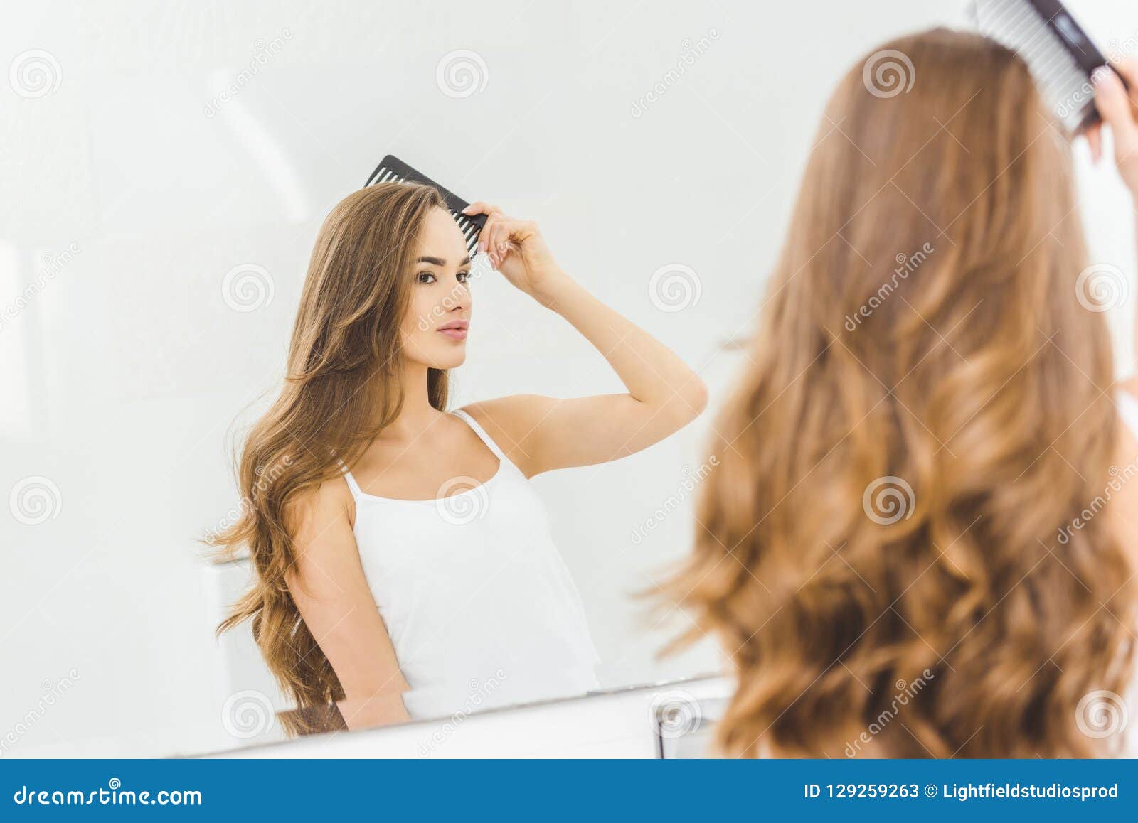 Härlig kvinna som borstar hår med hårkammen i badrum